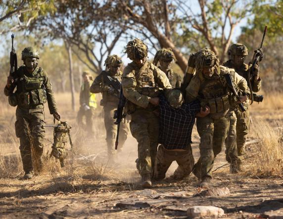 Caption: Australian Army soldiers from the 5th Battalion, The Royal Australian Regiment, carry a simulated enemy casualty to the collection point, while a Philippine Army soldier (left) carries the casualty's gear, following a firefight during Exercise Predator's Run at the Bradshaw Field Training Area.